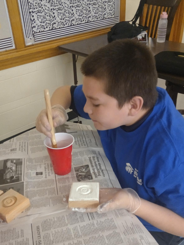 A student dipping his paint brush into water as he paints on his rosette corner block.