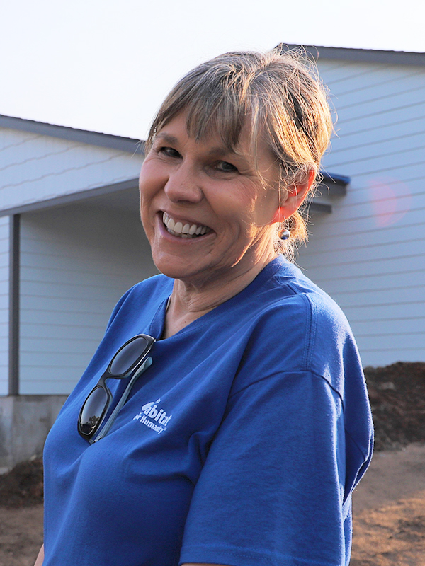 Board member Ann standing in front of a constructed home.