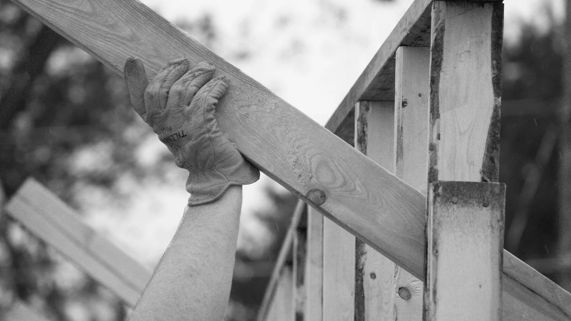 Black and white close-up of a gloved hand gripping a wooden beam during construction.