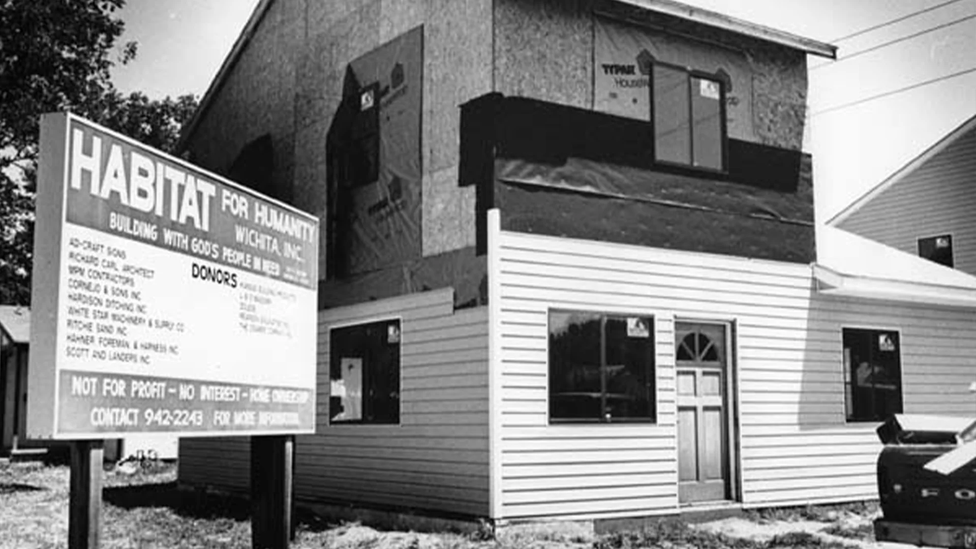 Black and white photo of a two-story Habitat home under construction with a large donor sign in the front yard.