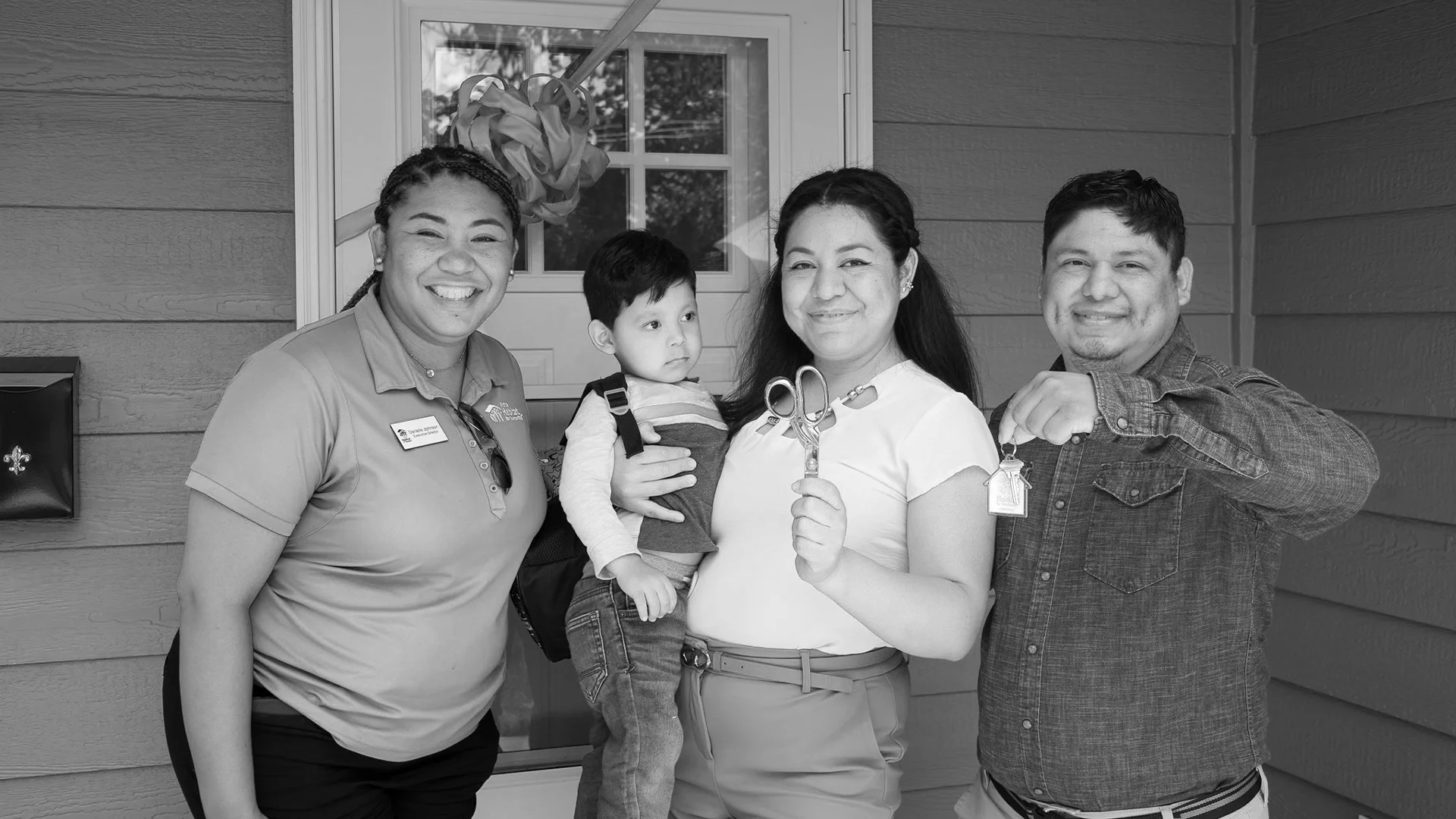 Wichita Habitat Executive Director Danielle Johnson poses with a smiling family of three holding house keys and ceremonial scissors at their home dedication.