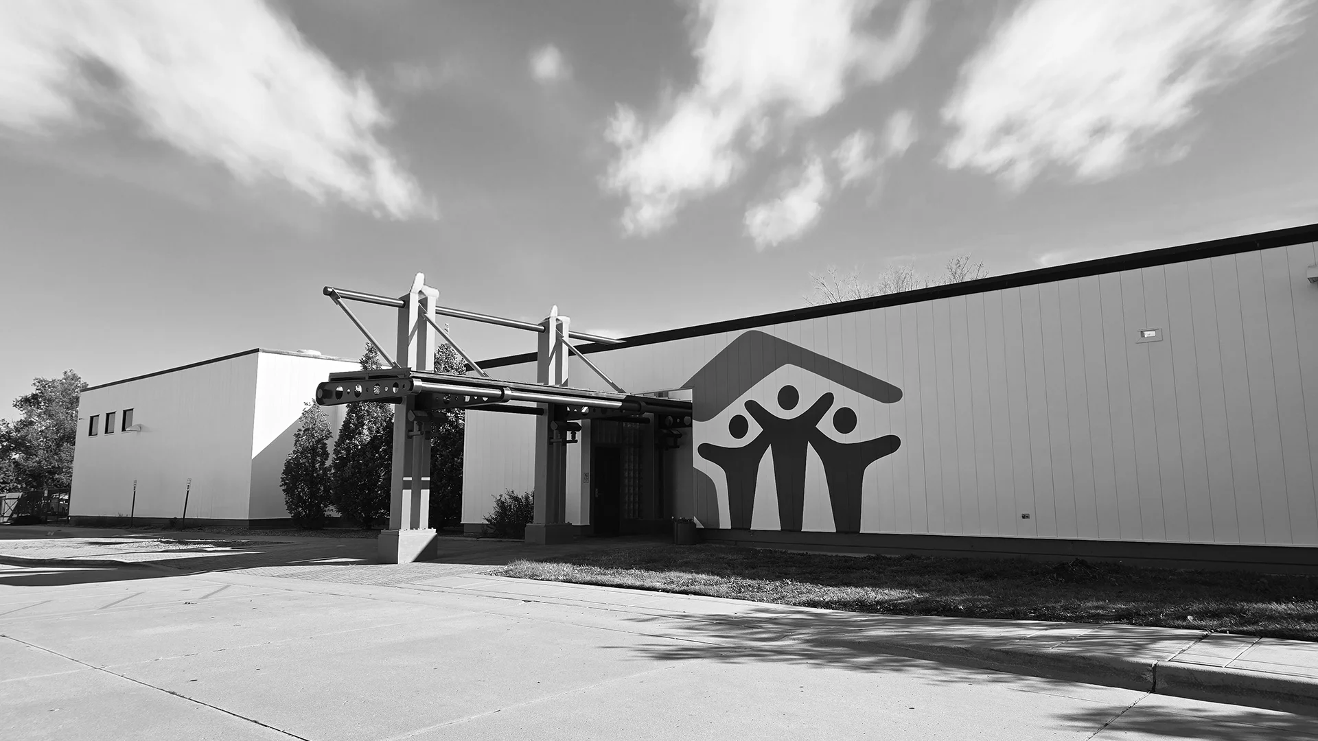 Black and white exterior view of the Wichita Habitat for Humanity building featuring a large logo mural and a modern metal entrance awning.