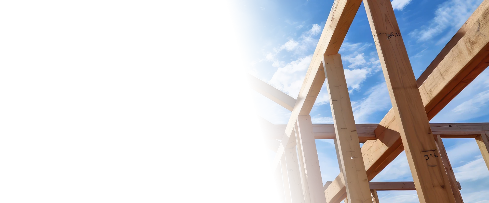 Wooden frame of a house under construction against a bright blue sky with sun glare.