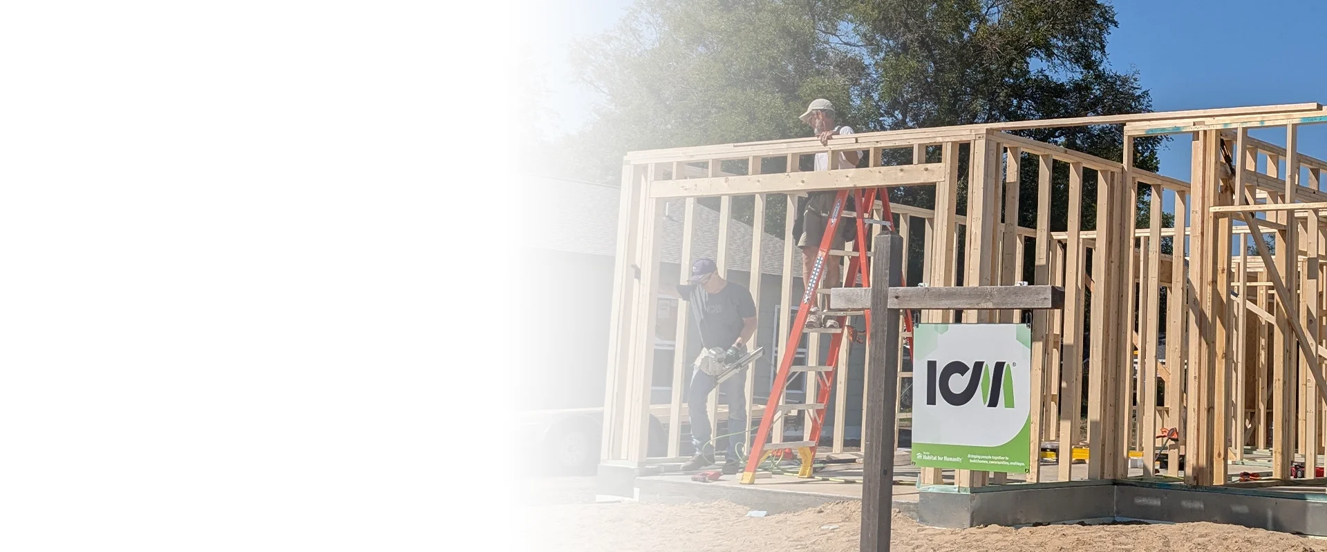 Volunteers working on the wooden framing of a house at a construction site with an ICM sign in the foreground.