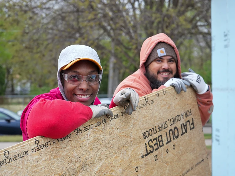 Family partners Candice and Chat smiling together while carrying wooden planks.