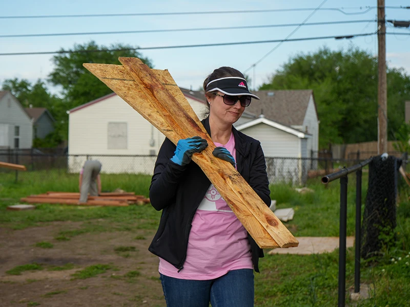 A volunteer carrying wood over their shoulder.