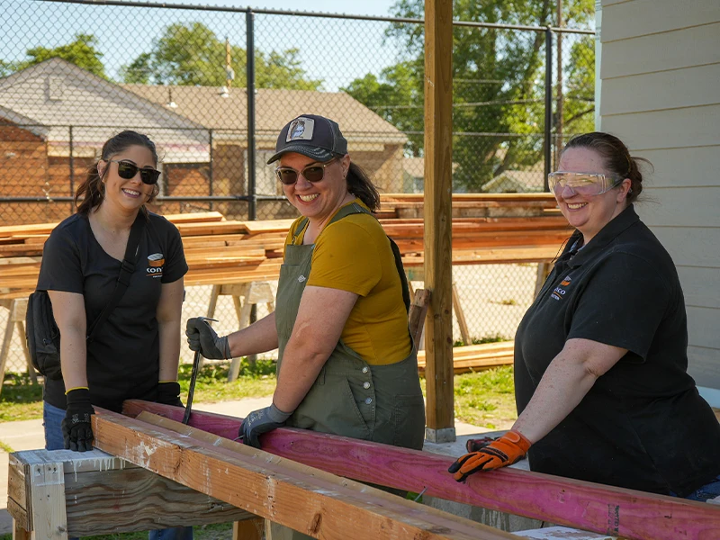 Three volunteers separating two wood lumber apart using a cat claw.