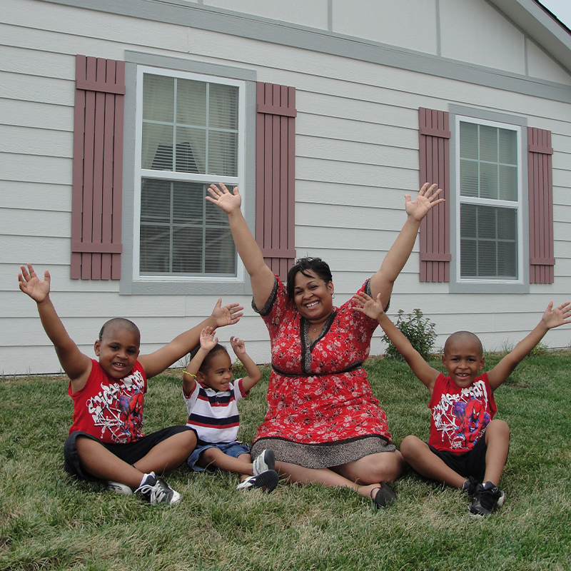 Mother and children raising their arms while sitting on the grass in front of their home.