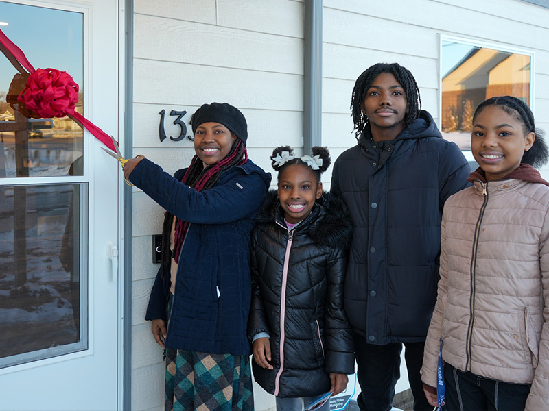 Family partner Naomi and her children cutting the ribbon at the home dedication ceremony.
