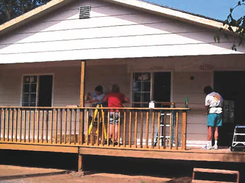 A small, single-story white house with a wooden front porch and steps.