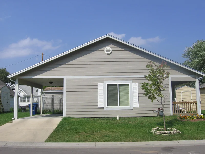 A small single-story gray house with a carport and trees.