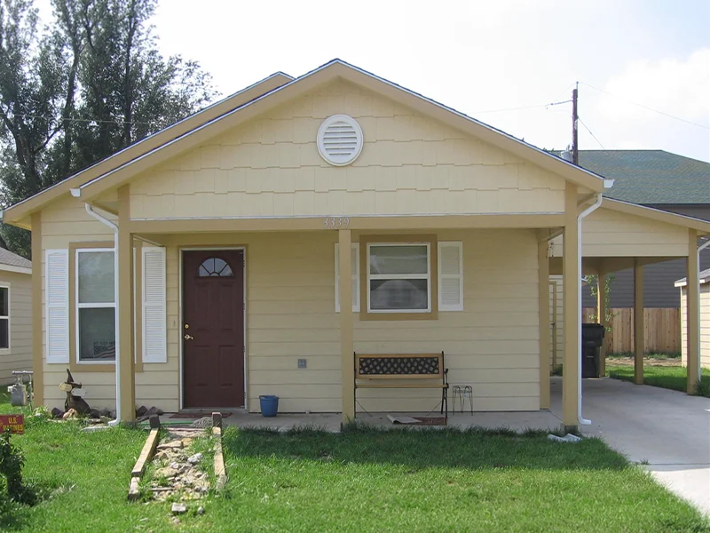 A small, single-story yellow house with a carport.