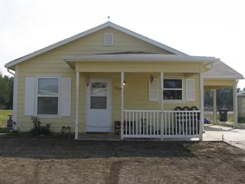 A small, single-story yellow house with a carport and front porch.