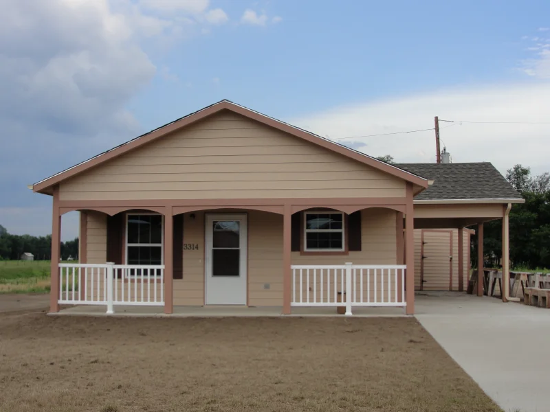 A small, single-story tan house with a carport and front porch.