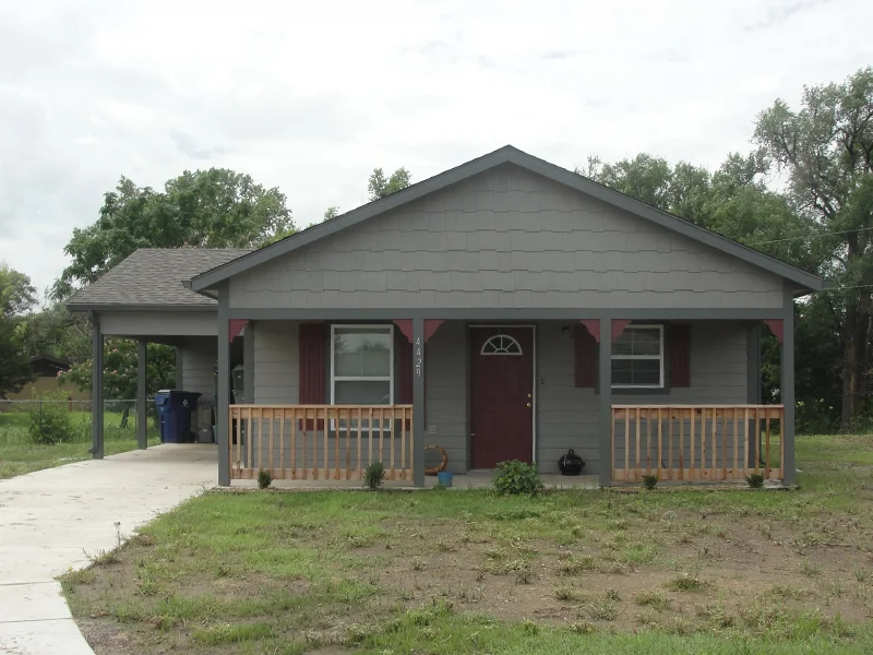 A small, single-story dark gray house with a carport and front porch.