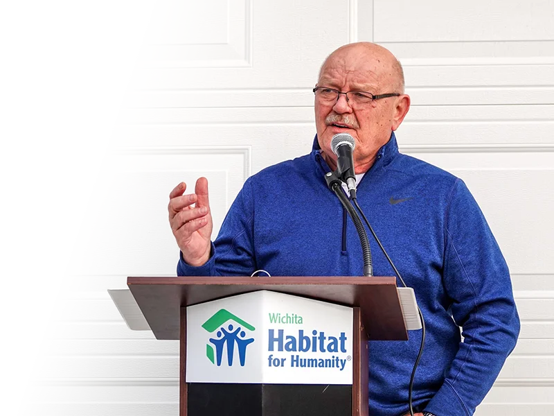 Dave VanderGriend speaking at a podium in front of a white garage door.