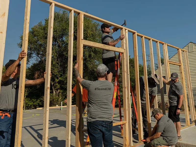 ICM employees helping to raise a wall at a future Habitat home construction site.