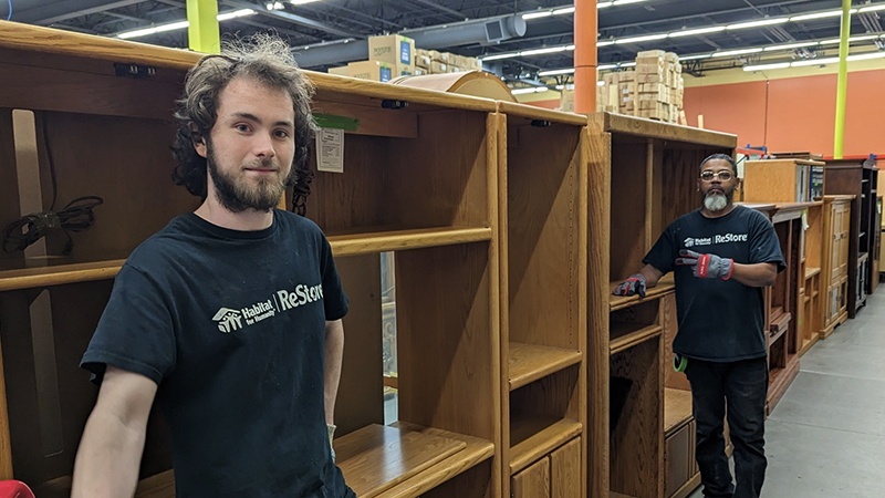 Two ReStore employees standing in front of entertainment centers.