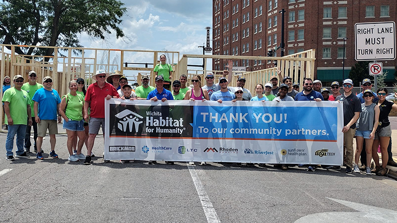 A group of volunteers standing in front of the completed walls and behind a banner.
